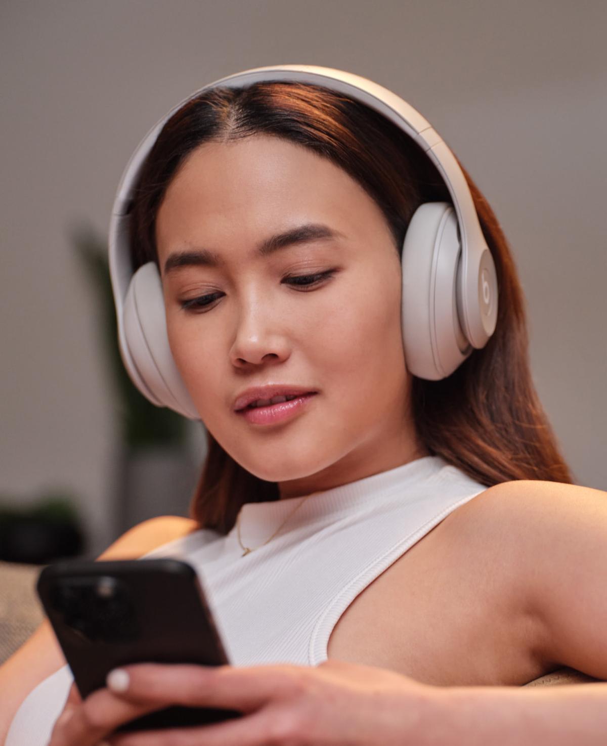 Woman wearing Beats Studio Pro checking phone — noise cancellation in use